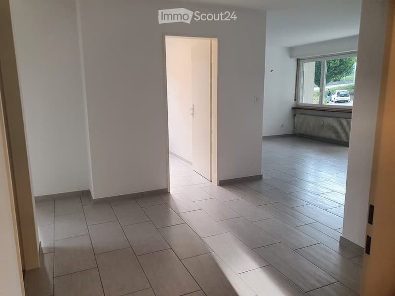 Empty hallway with white walls, grey tiles, and an open door.