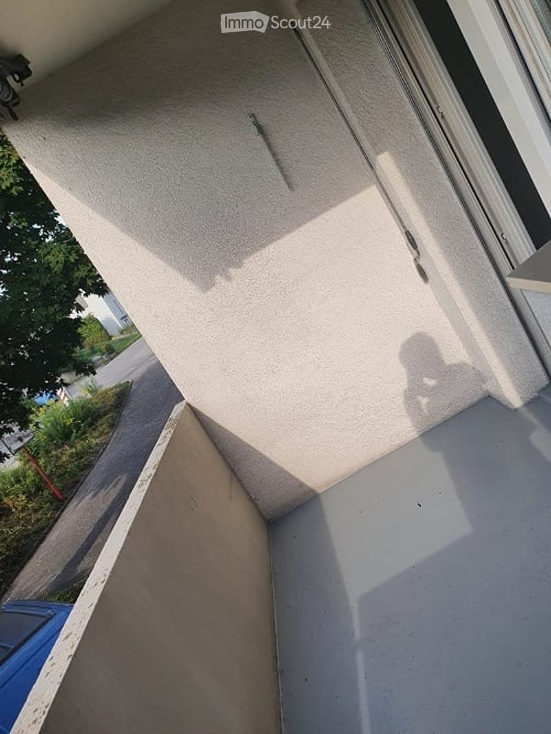 A balcony or terrace with a concrete floor and a white wall, visible shadows of person