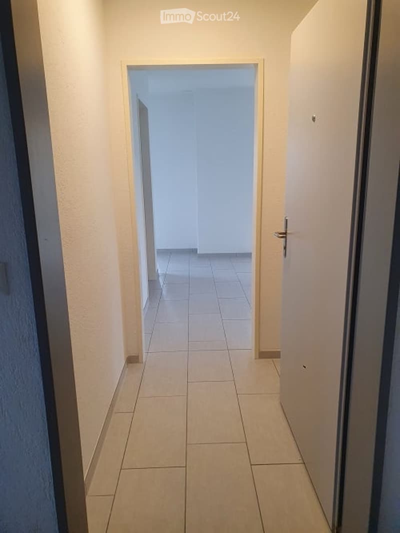 An empty corridor with light-colored tile flooring, two doors, and neutral walls.