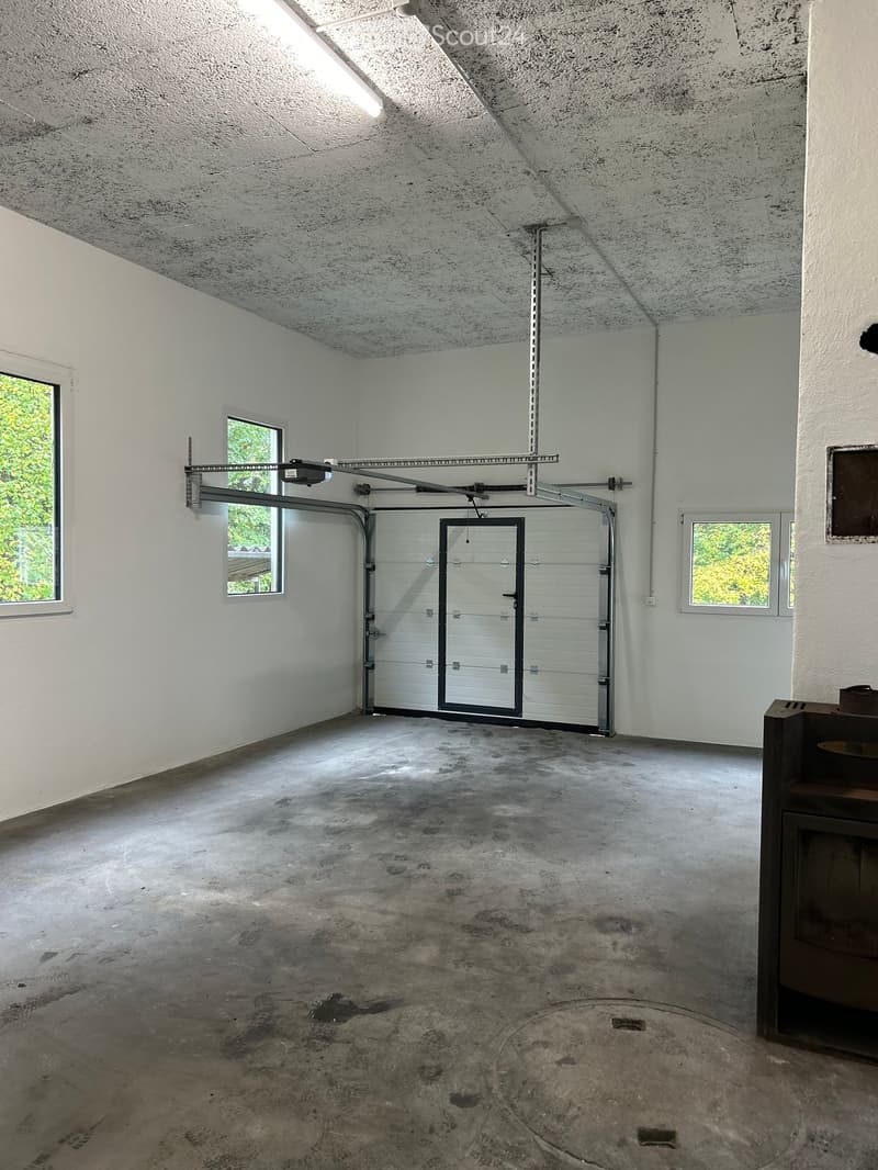 Empty garage with white walls, concrete floor, and a large overhead door. Windows on two walls provide natural light.