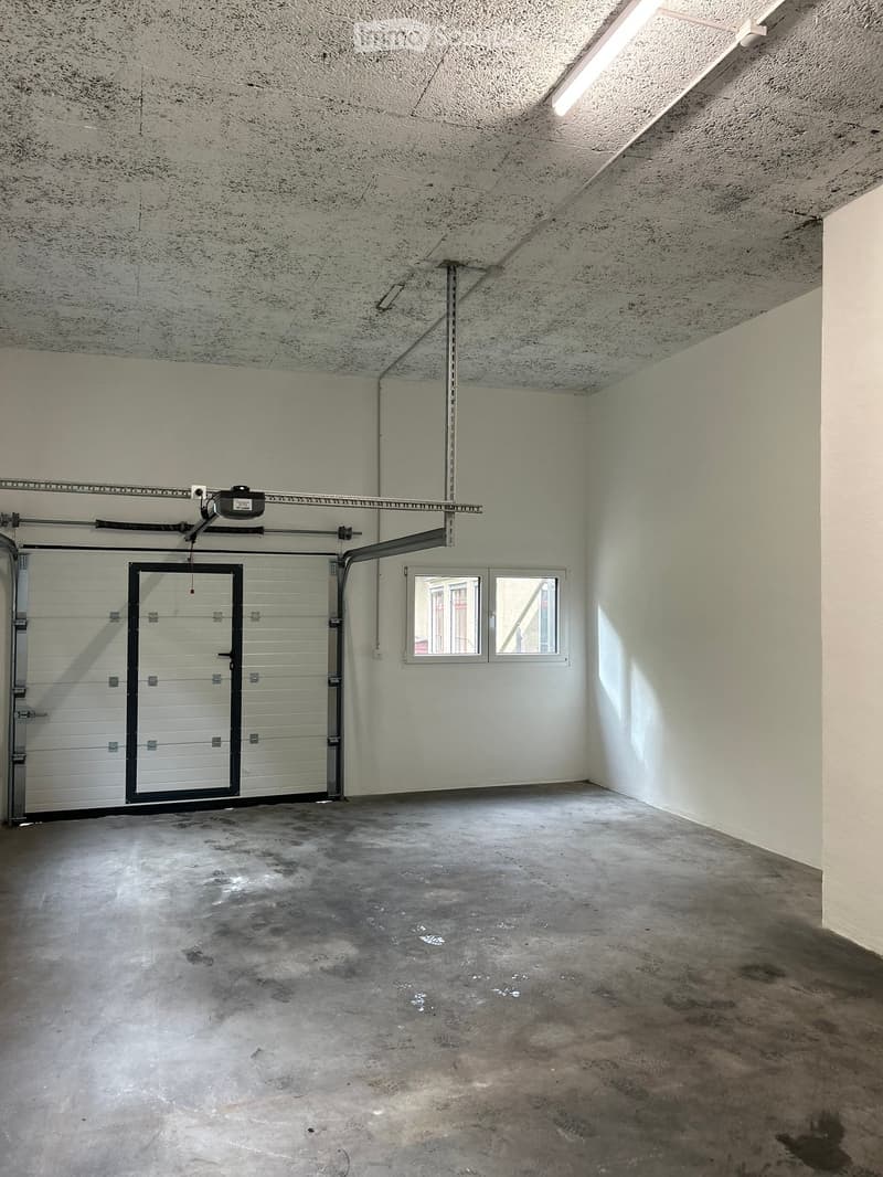 Empty garage with concrete floor, white walls, garage door, and small window.