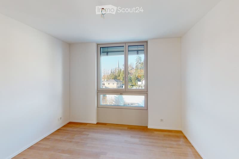an empty room with wooden floor and white walls, a large window, and no furniture