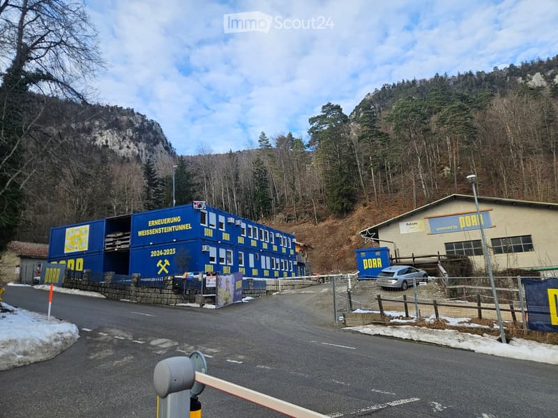 Blue building with yellow signs, a parked car, mountainous landscape, road, and snow on the ground.