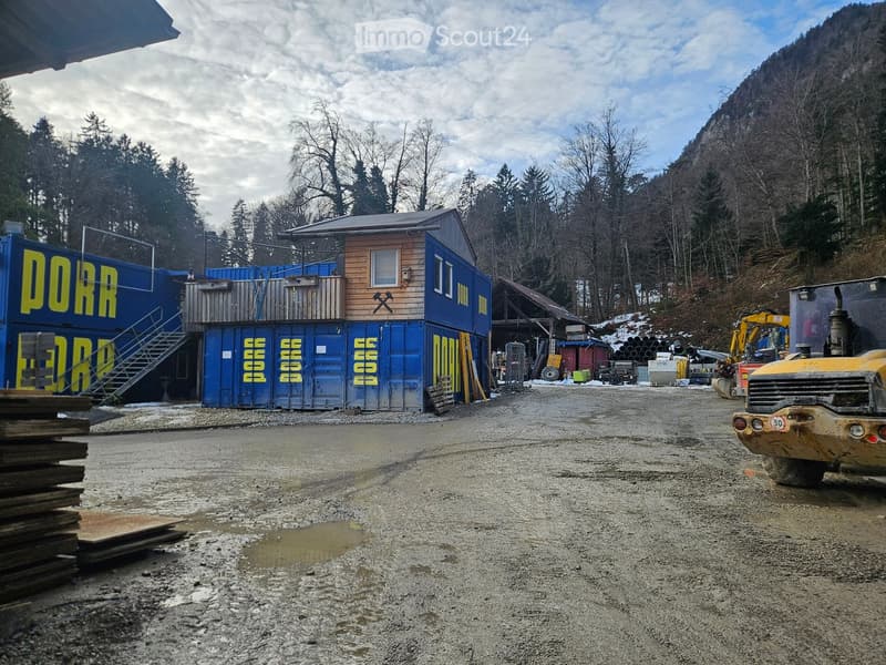 small rustic wooden cabin with blue walls, surrounded by blue container buildings, set in a mountainous forest area