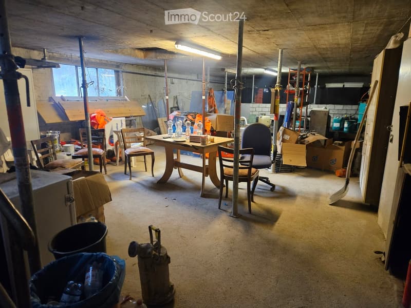 Basement room, bare concrete walls, large windows, wooden desk, chairs, storage boxes, metal rods