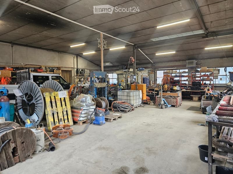 Empty warehouse with various industrial equipment, storage racks, and a truck parked inside.