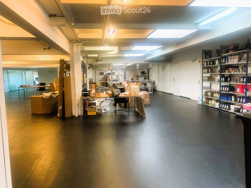 large empty room, ceiling lights, storage boxes, tables with items, racks with items, tables in distance