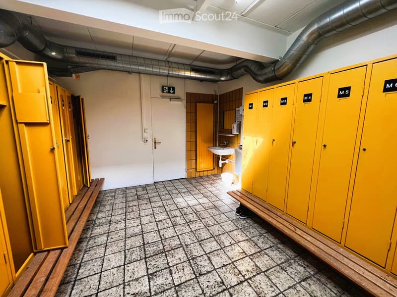 Empty yellow locker room with benches, sinks, pipes, and a door
