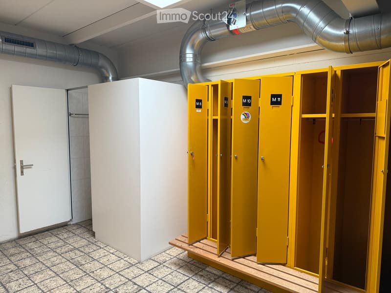Empty room with tiled floor, white walls, and several yellow lockers with open doors. A white cabinet is visible on the left side.