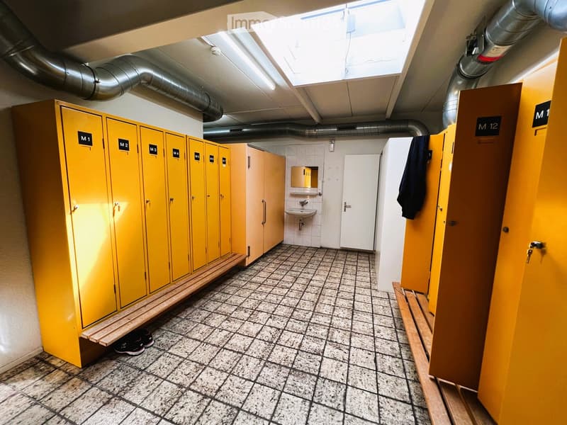 A yellow locker room with multiple yellow lockers, a bench, and a sink area, along with a door and a window.