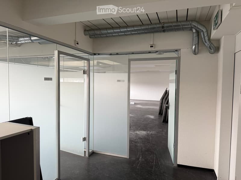 Modern hallway with glass partitions, white walls, dark flooring, and visible ceiling pipes.
