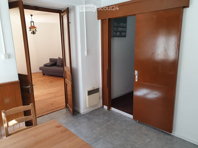 Wooden table and chair, wooden door, wooden floor, couch with pillows, radiator