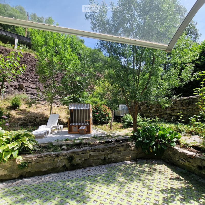 Outdoor lounge area with lounge chair, covered seating, stone pavement, greenery
