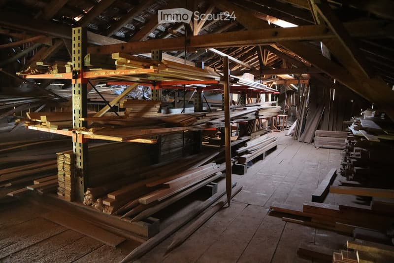 High ceiling storage room with wooden beams and shelves filled with wooden planks and lumber.
