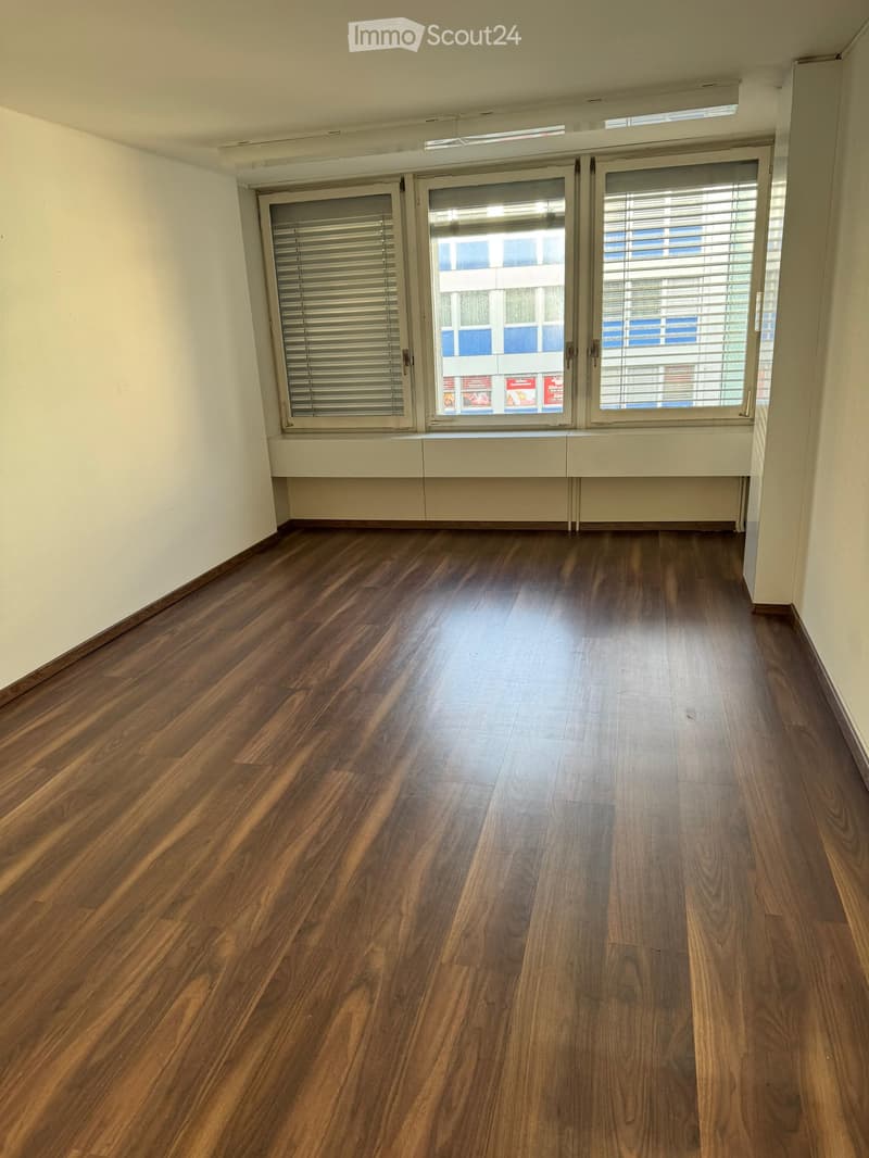 Empty room, wooden flooring, white walls, large windows, closed shutters, city view