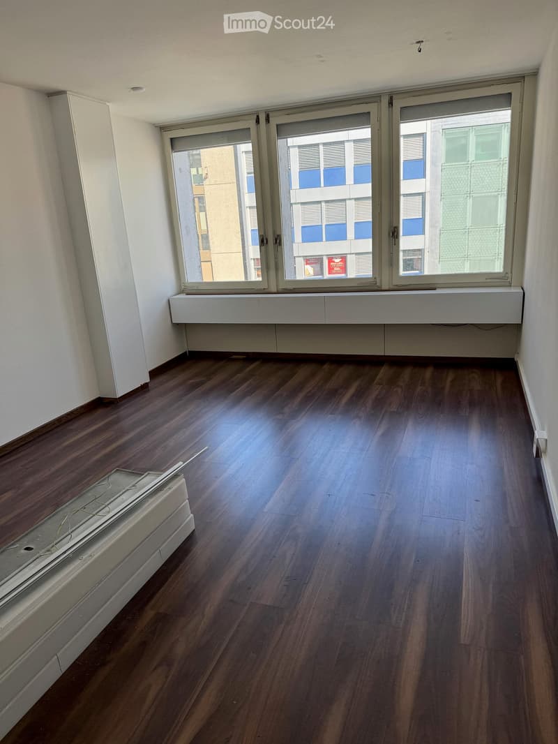 Empty room with wooden flooring, white walls, and large windows with blinds. Radiator visible under the windows.