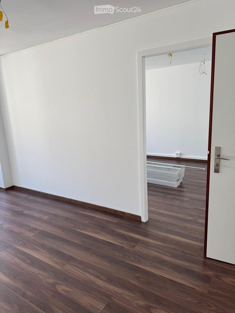 Empty hallway with wooden flooring and white walls, featuring a doorway leading to another room with a radiator visible.