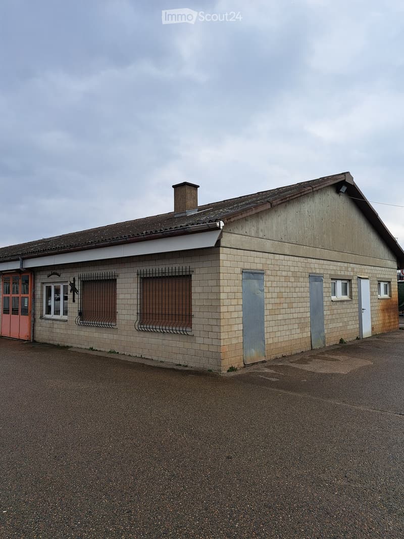 Industrial building with brick walls, a brown roof, large windows, red entrance door, metal shutters, metal doors, and chimney