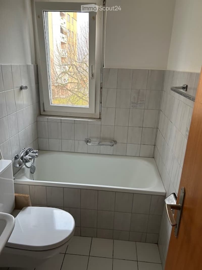 Bathroom with a white bathtub, toilet, and a window with a view of a building outside.