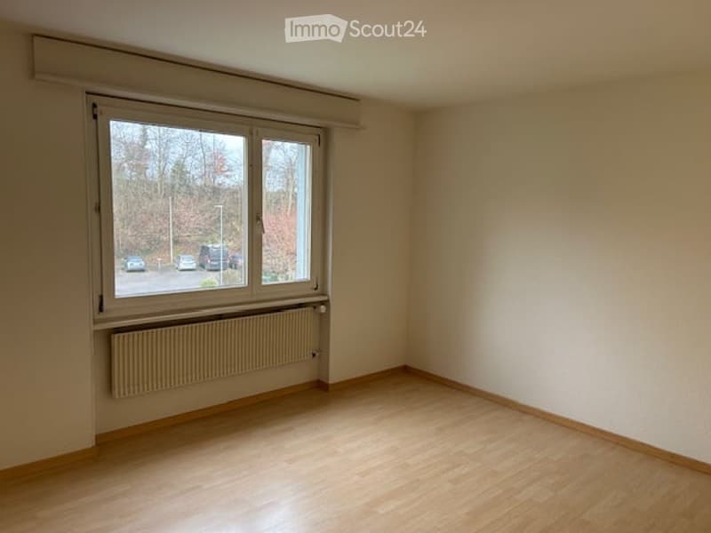Empty room with wooden flooring, large window, radiator, and bare walls.