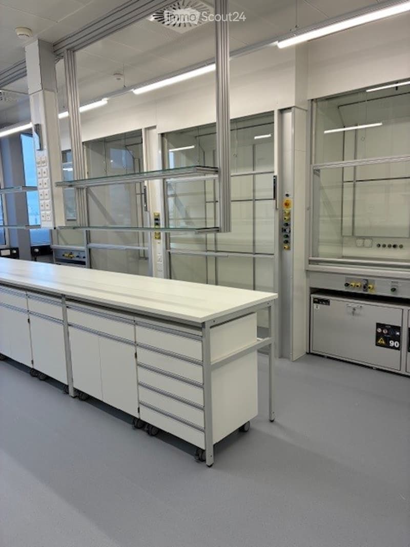 White laboratory equipment, gray floors, overhead lighting, glass cabinets, steel shelves