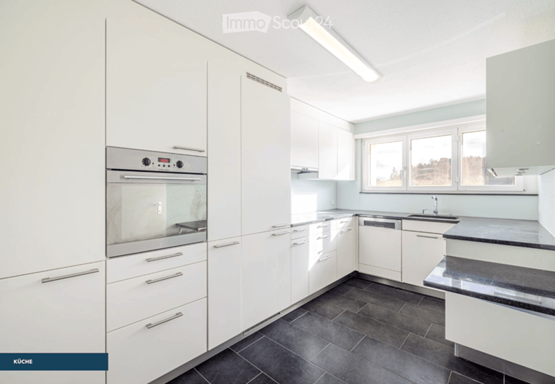 Modern kitchen with white cabinets, black countertops, and stainless steel appliances including an oven and dishwasher. The space features large windows and a sleek, contemporary design.