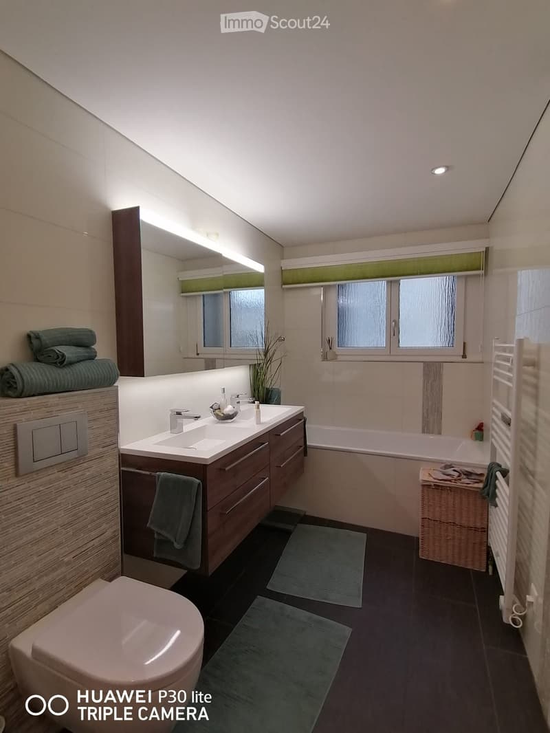 modern bathroom with bathtub, double sinks, toilet, wooden cabinets, white tiles, towel warmer