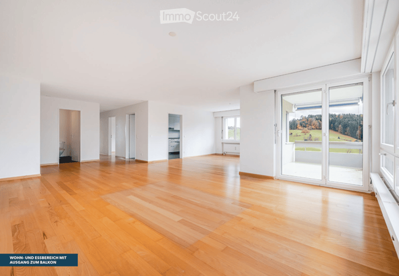 Empty room with wooden flooring, white walls, large sliding glass doors leading to a balcony, and visible doorways to other rooms.