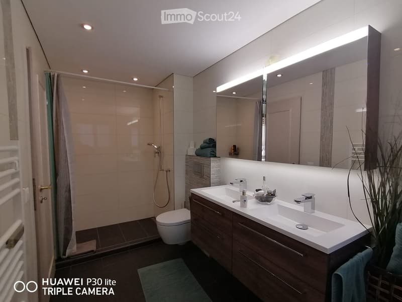 modern bathroom with double sink, mirror, toilet, shower stall, and wooden cabinets
