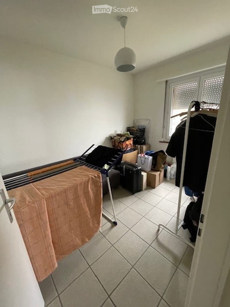 room with iron, folding table, boxes, hanging clothes, plastic bag
