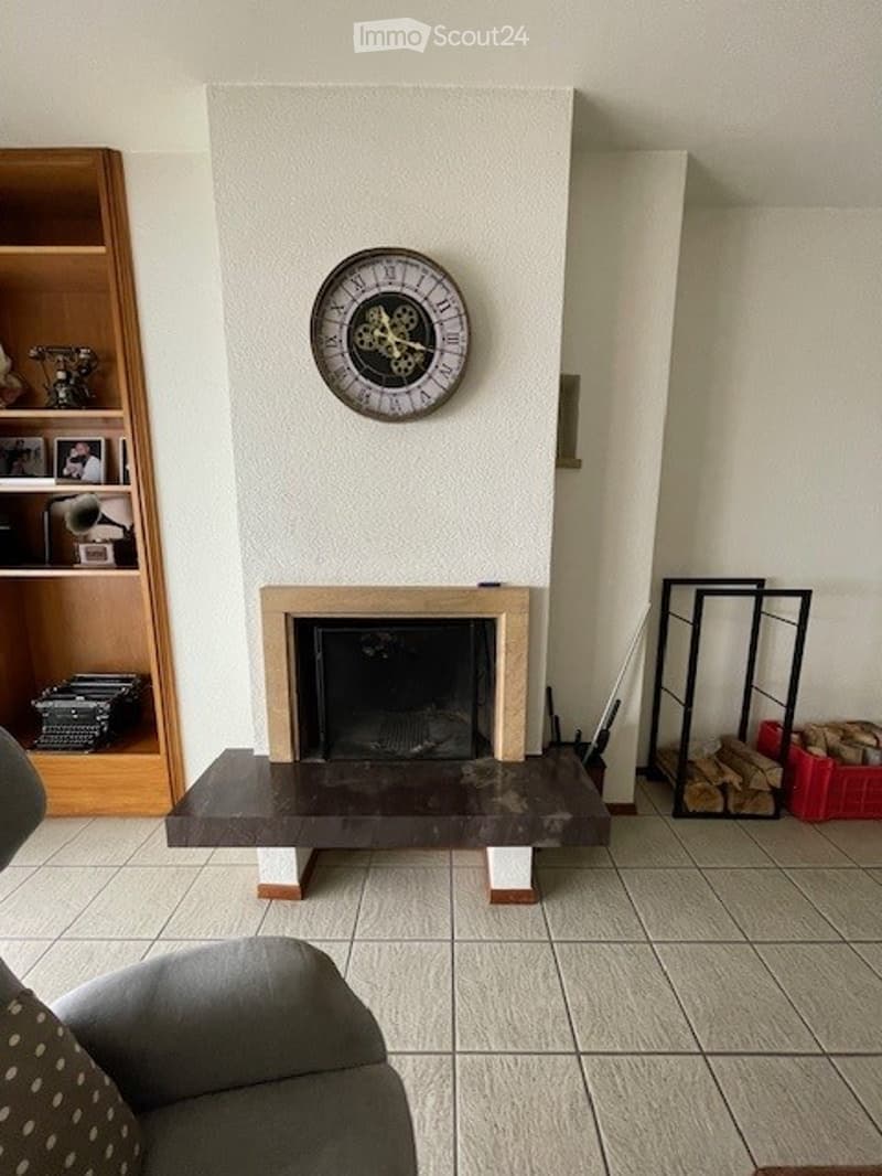 A room with a fireplace, white walls, a tiled floor, a wooden shelf, a couch, and a decorative clock.
