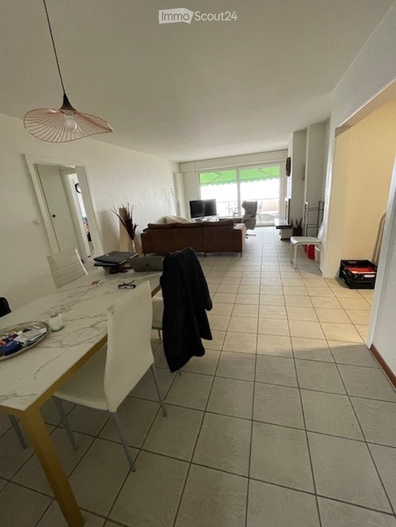 Dining area with a table and chairs, white tiled floor, living room with couch and table