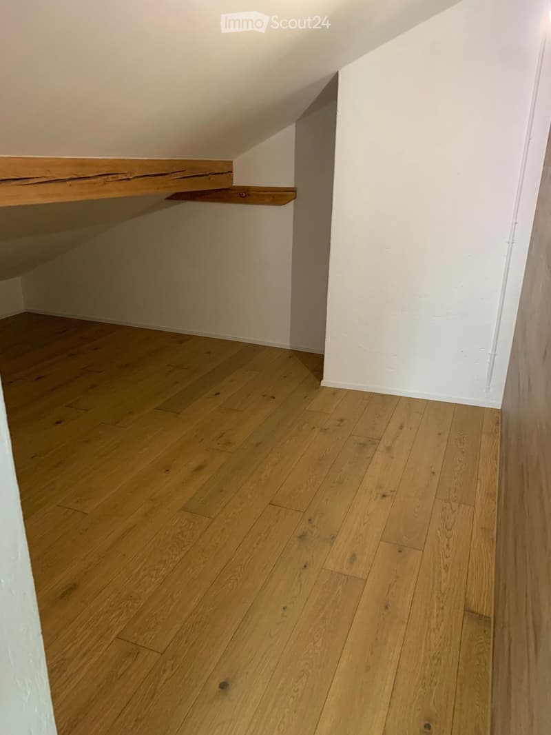 empty attic room with wooden flooring and wooden beams on the ceiling