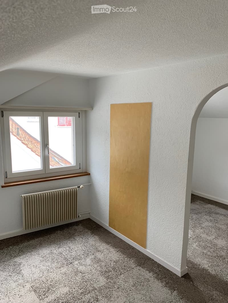 Empty room with window, heater, beige wall, and carpeted floor.