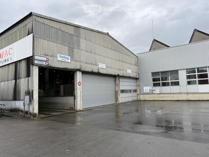Industrial building, metal siding, white exterior, large open garage doors, paved parking lot, adjacent building