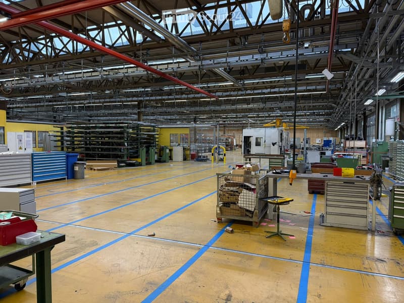 Large industrial warehouse with yellow painted walls, industrial machinery, carts, and tables with equipment