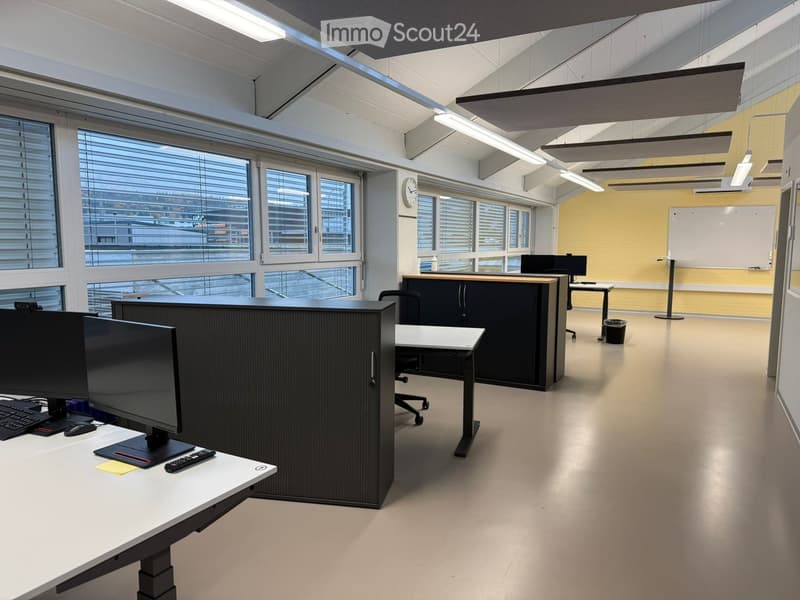 Empty office room with glass windows, black office cubicles, desks, monitors, keyboards, whiteboard on wall, trash bin