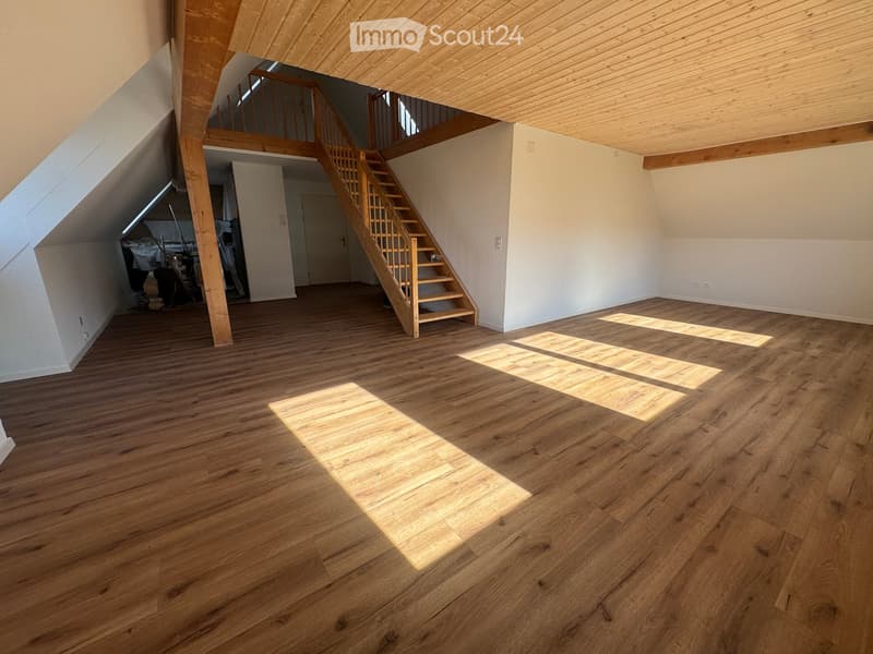 Empty room with wooden floor, white walls, wooden staircase, beams in the ceiling