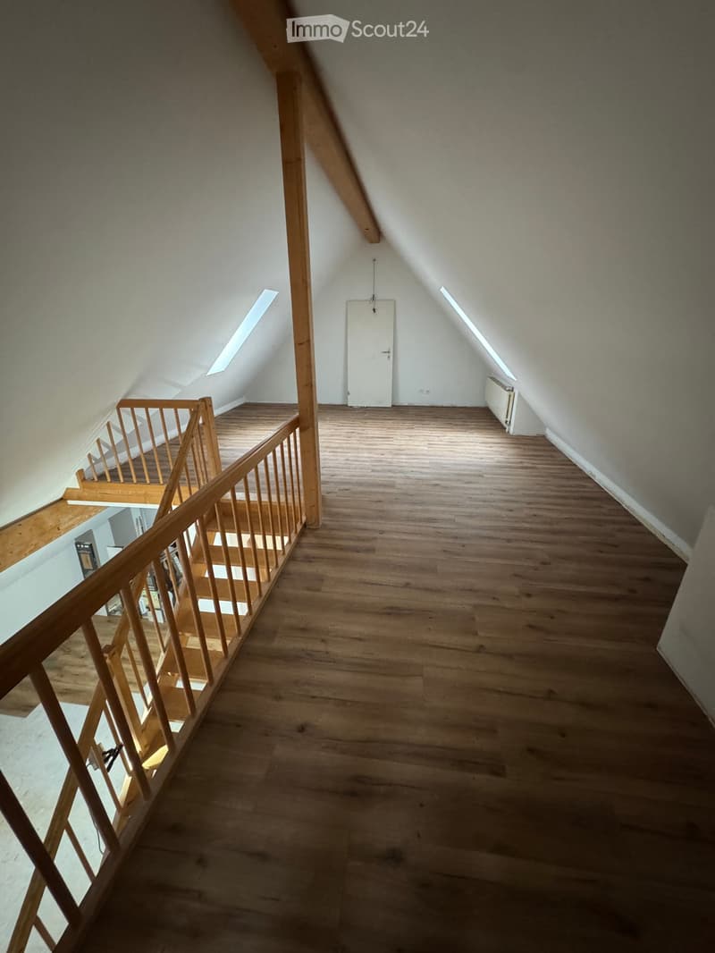 An empty attic room with wooden staircase and floor, white walls, and white door