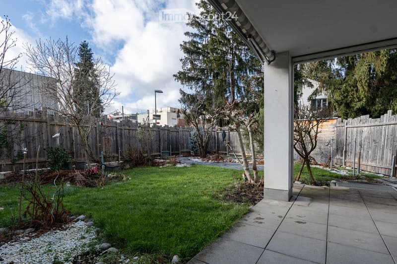 large paved area, wooden fence, green lawn, trees, plants