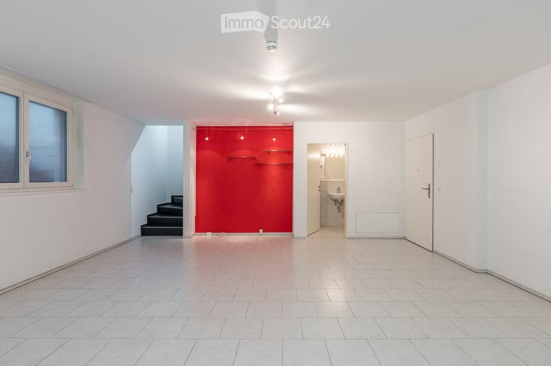 Empty room with white tiled floor, white walls, large red wall, white ceiling with lights, window, and staircase.