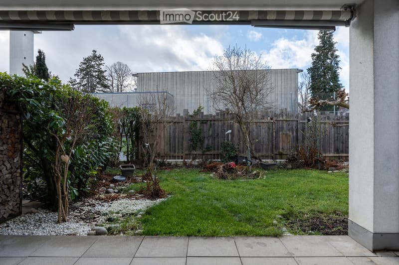 small garden with plants, shrubs, and trees, wooden fence, paved ground, green grass, a shed