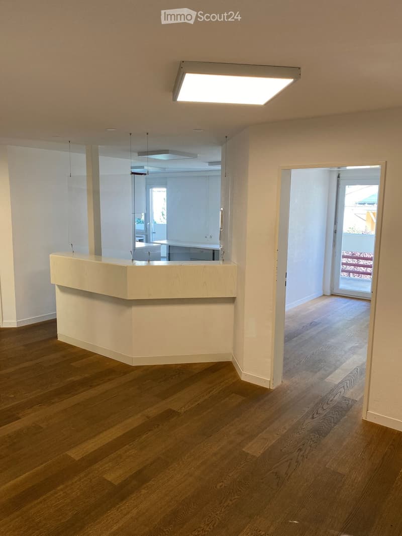 Empty room with wooden floor, a long white counter, glass wall, and bright ceiling light