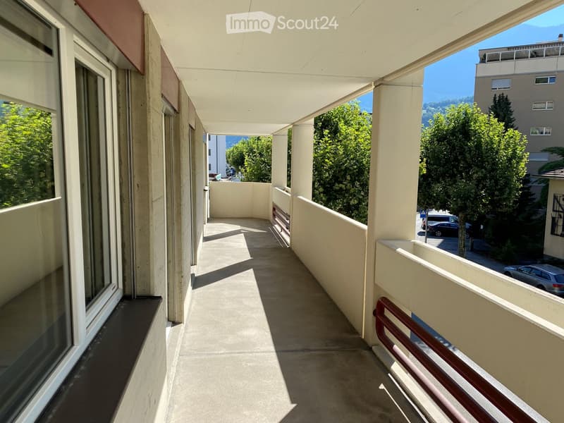 balcony with red railings, concrete floor, trees, parked cars, mountains