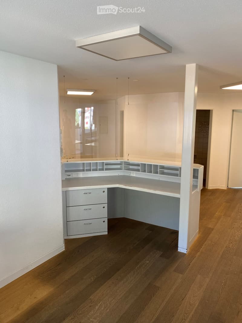 Corner office desk, glass partition, white cabinets, drawers, overhead lighting, wooden floor.