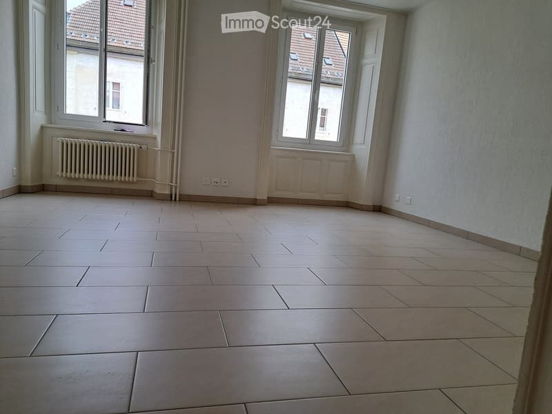 empty room with white walls, large windows, tiled floor, wall-mounted radiator