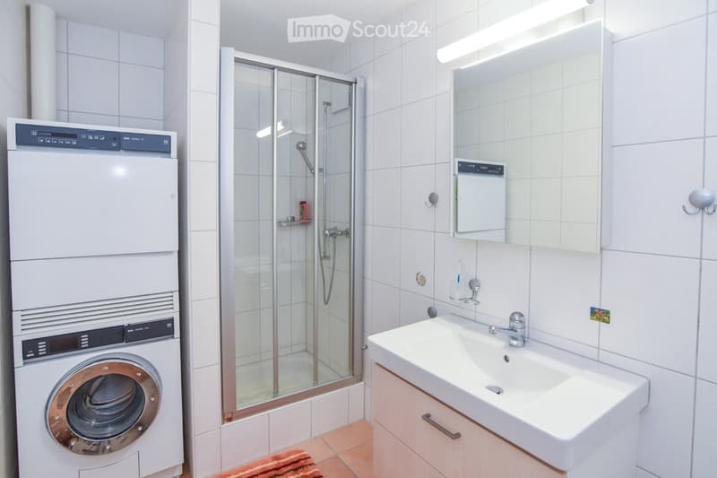 modern bathroom with tiled walls, white sink, mirror, shower, washing machine