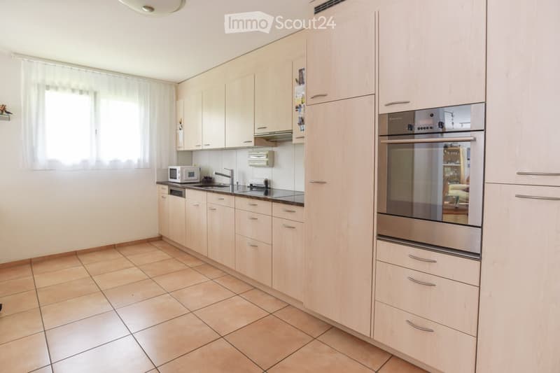 Modern kitchen with wooden cabinets, tiled floor, black countertop, stainless steel appliances, white microwave, open window with white curtains