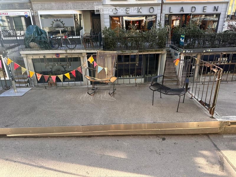 outside, cafe chairs, metal railings, stairs, flags hanging, plants on balcony