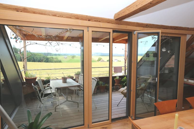 balcony, folding doors, table, chairs, decorative lights, view of a field